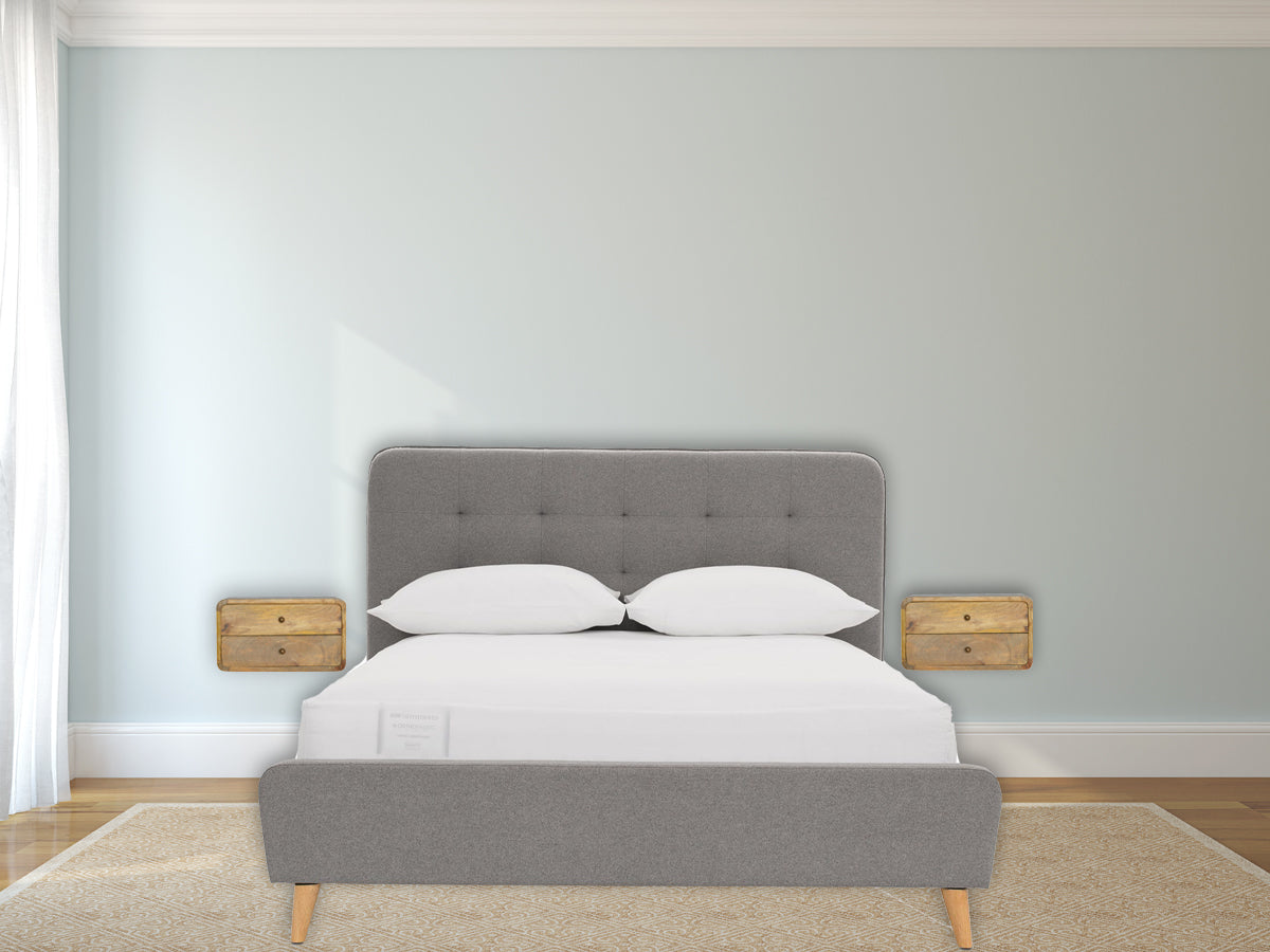 Oak-ish 2 Drawer Floating Nightstand with 2 drawers, shiny knobs, wall-mounted design, and solid mango wood. View of Nightstand mounted on opposite wall beside a bed